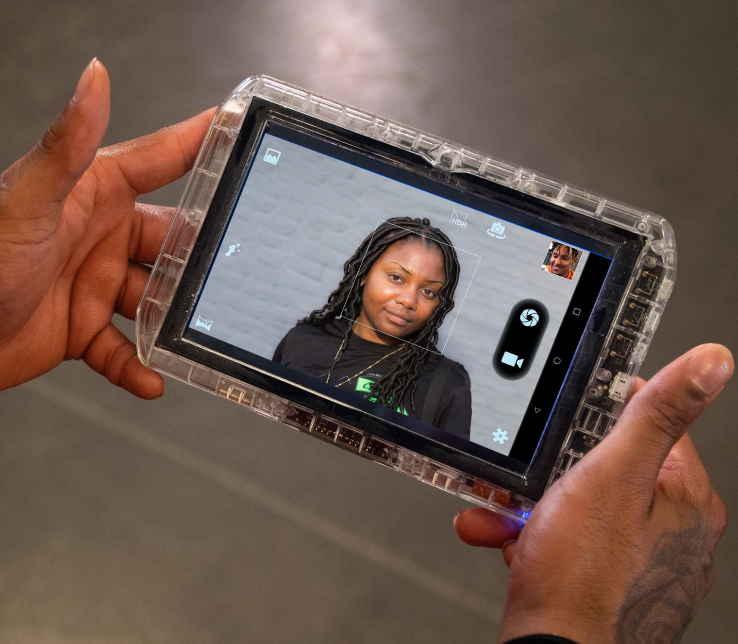 The image shows a person's face displayed on a handheld device, with the person's hands holding the device in the foreground.