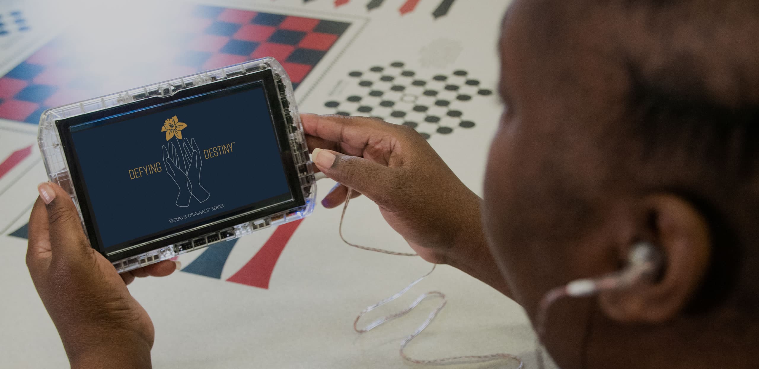 The image shows a person's hands holding a laptop displaying a character design on the screen, surrounded by various visual elements such as checkered patterns and dotted backgrounds.