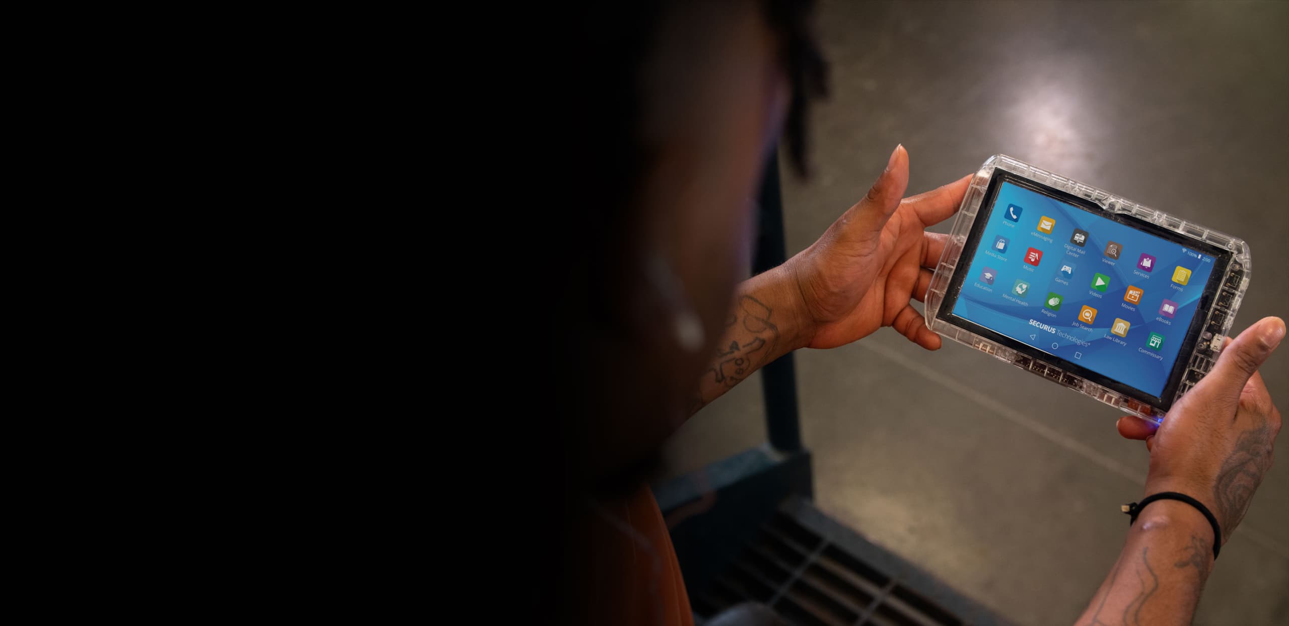 A person's hands holding a tablet device displaying various app icons in a dimly lit environment.