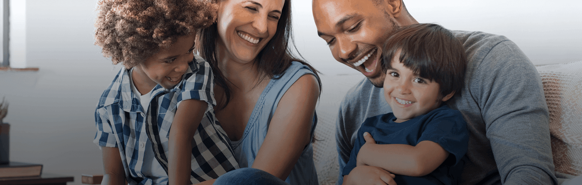 A happy family of four, including two adults and two children, are smiling and embracing each other in a warm and affectionate manner.