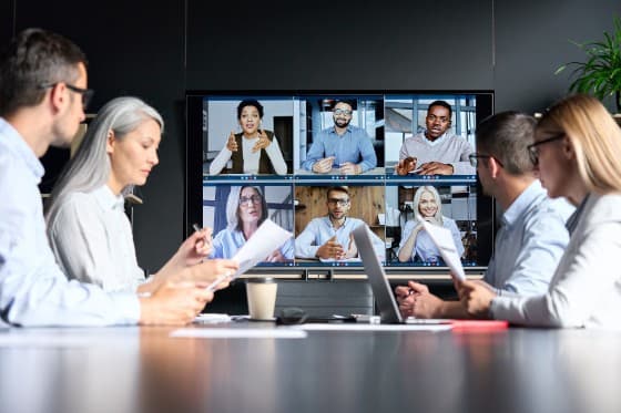 A group of people interacting via a large screen with multiple video call participants